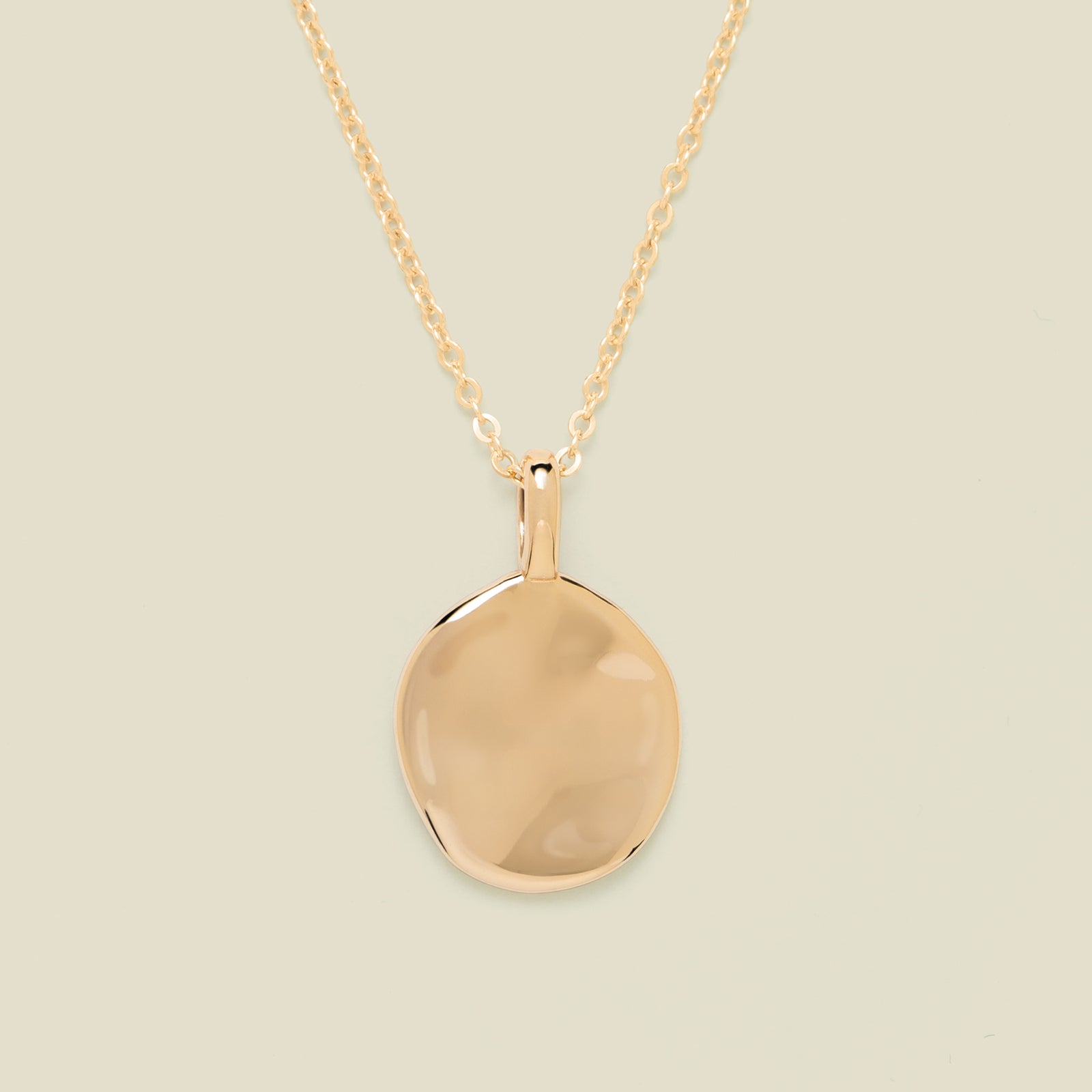 Gold necklace with disc pendant on beige background
