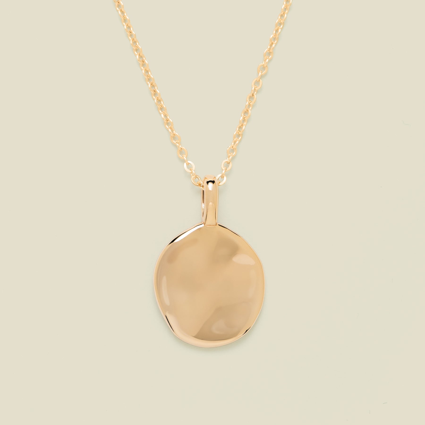 Gold necklace with disc pendant on beige background