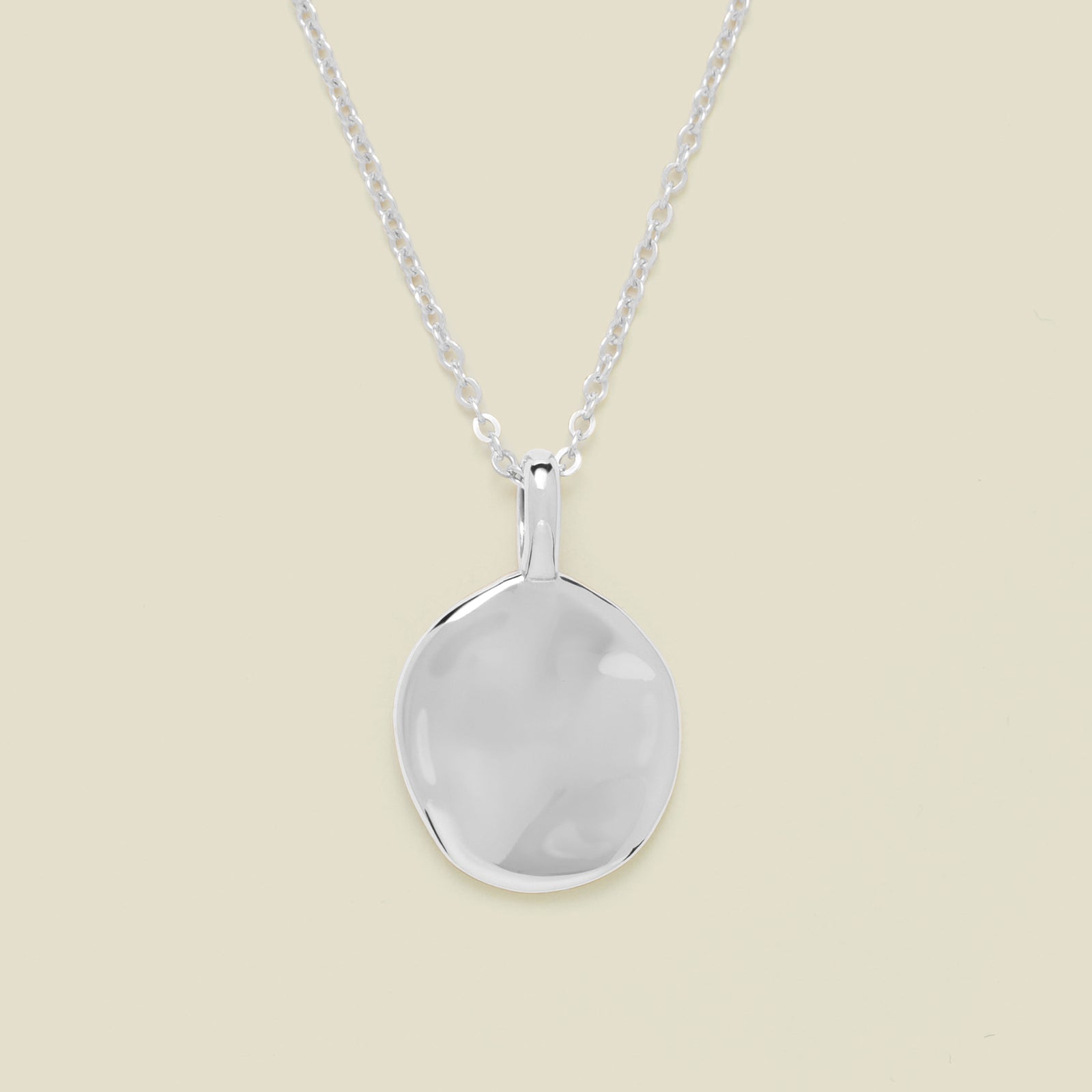 Silver necklace with a round pendant on a beige background