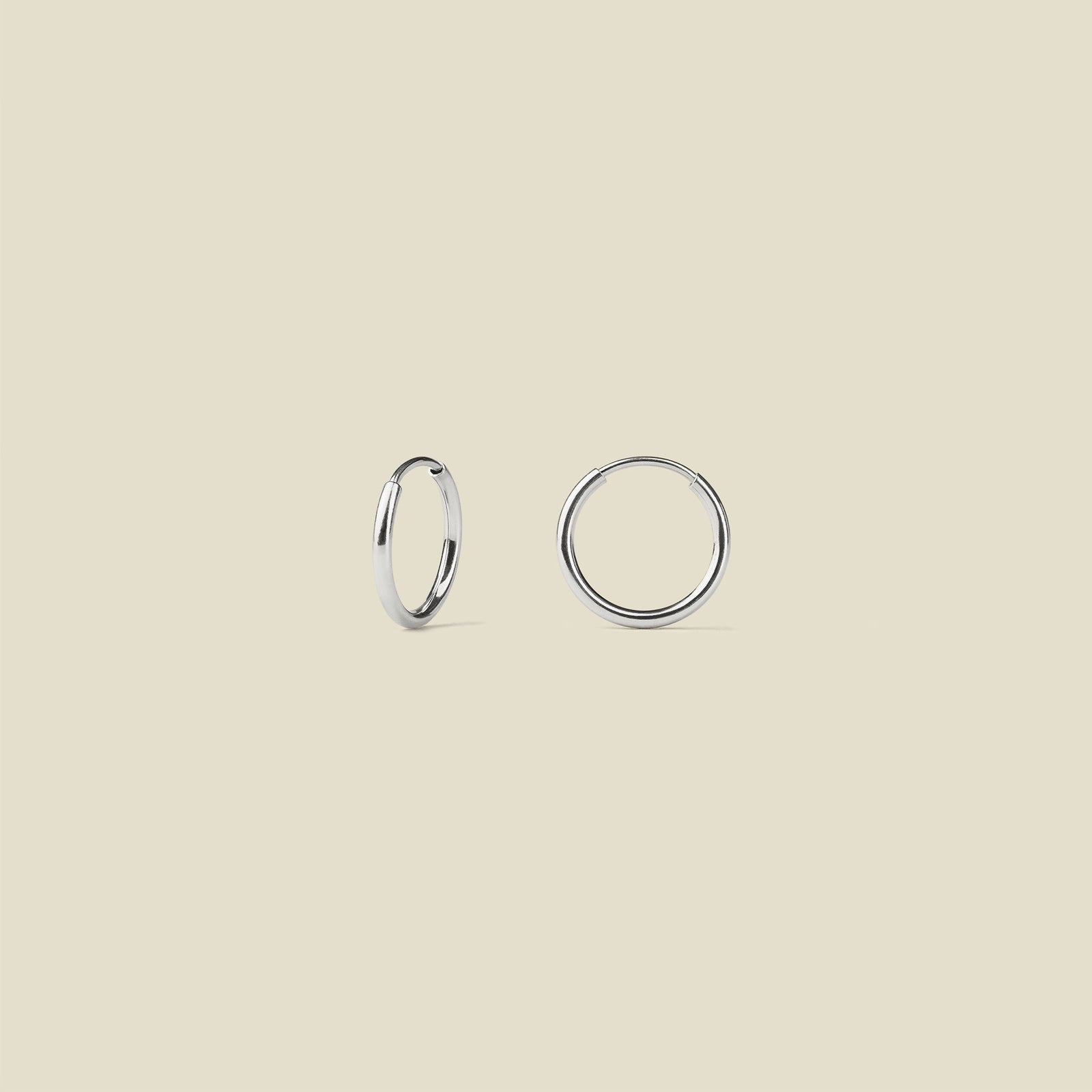 Two silver hoop earrings on a beige background