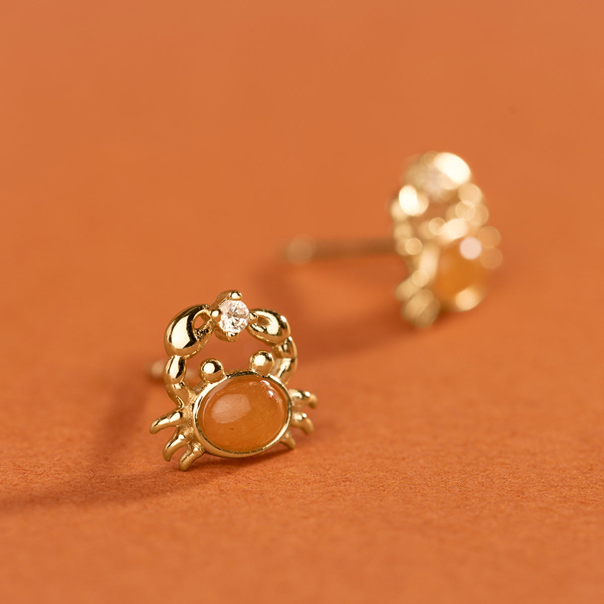 gold crab-shaped earrings with orange gemstone in the center on an orange background