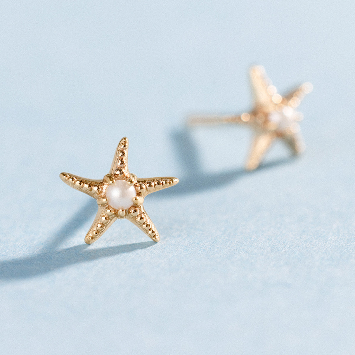 Gold starfish-shaped earrings with pearls on a light blue background