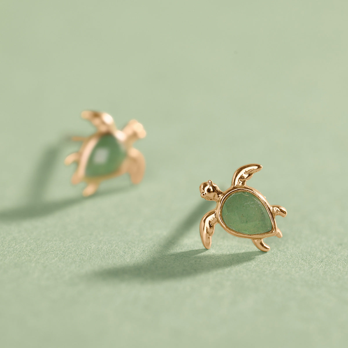 Gold turtle-shaped earrings on a light green background