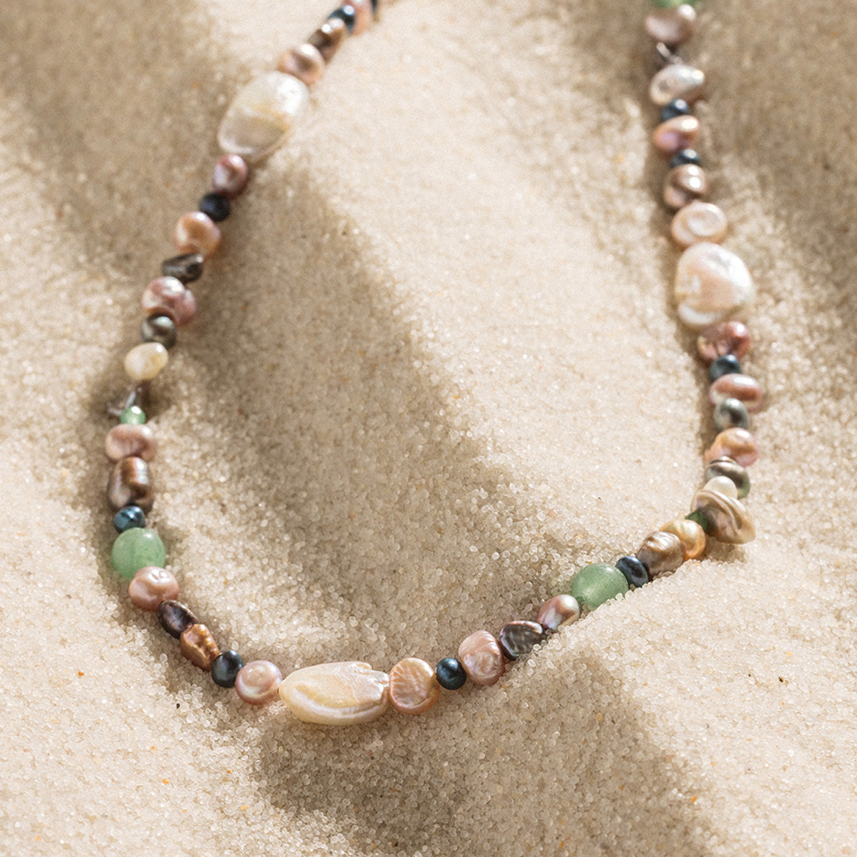 Necklace with multicolored pearls on a sandy surface