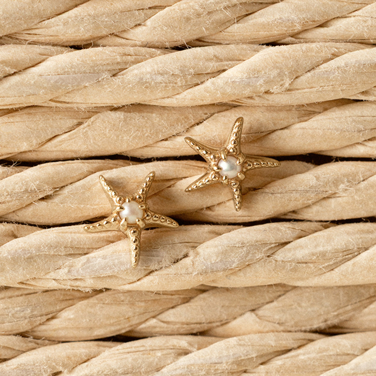 Gold starfish earrings with pearls on a woven beige background