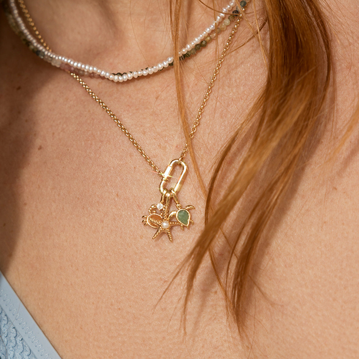 Close-up of a gold necklace with a turtle, starfish and crab charms worn by a model with red hair.