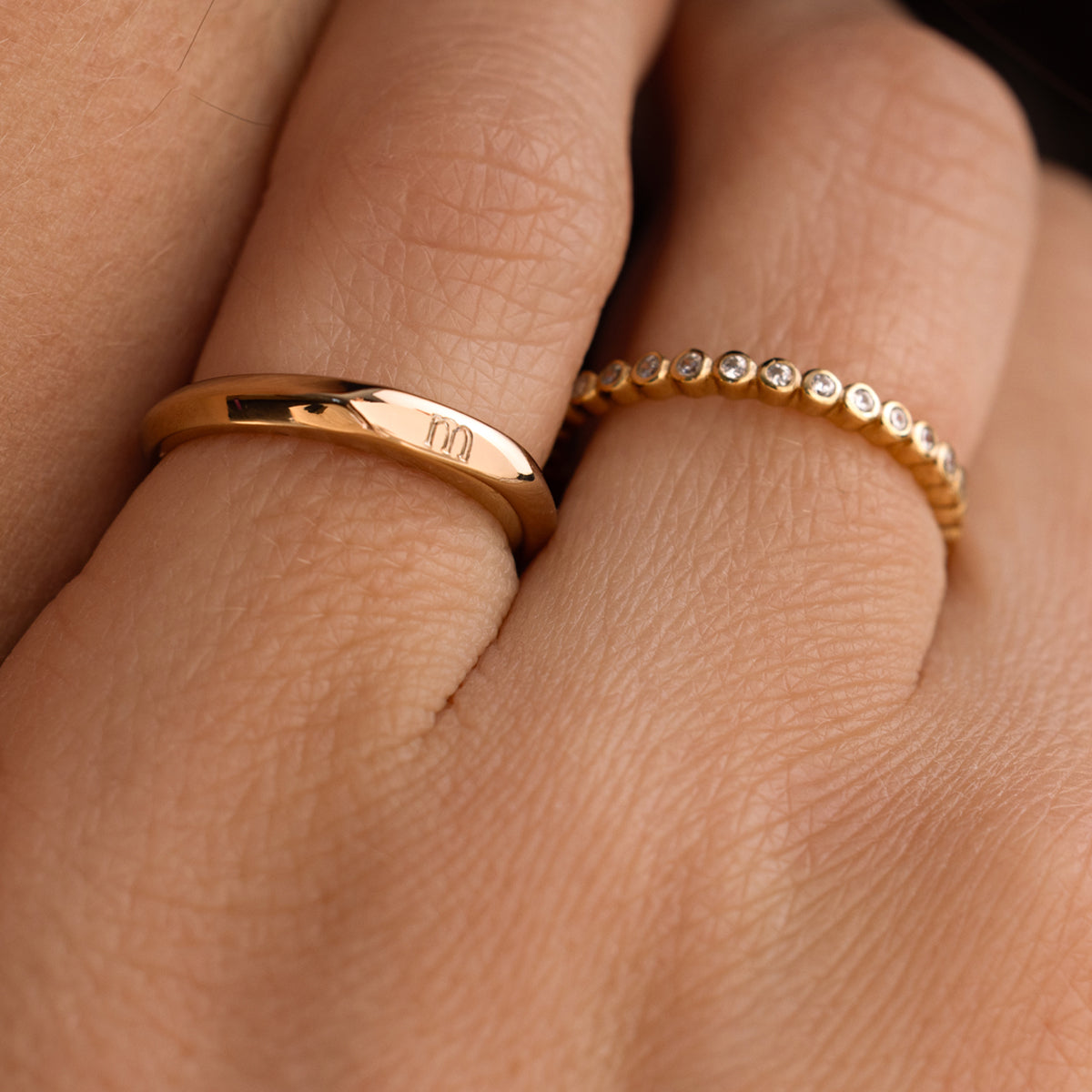 Close-up of a hand wearing two gold rings with diamond accents and engraved letter 'm'