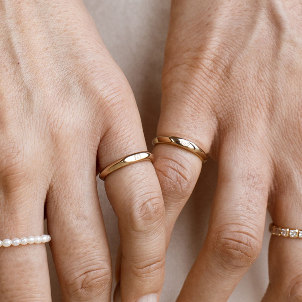 Close-up of two hands wearing gold rings on a neutral background