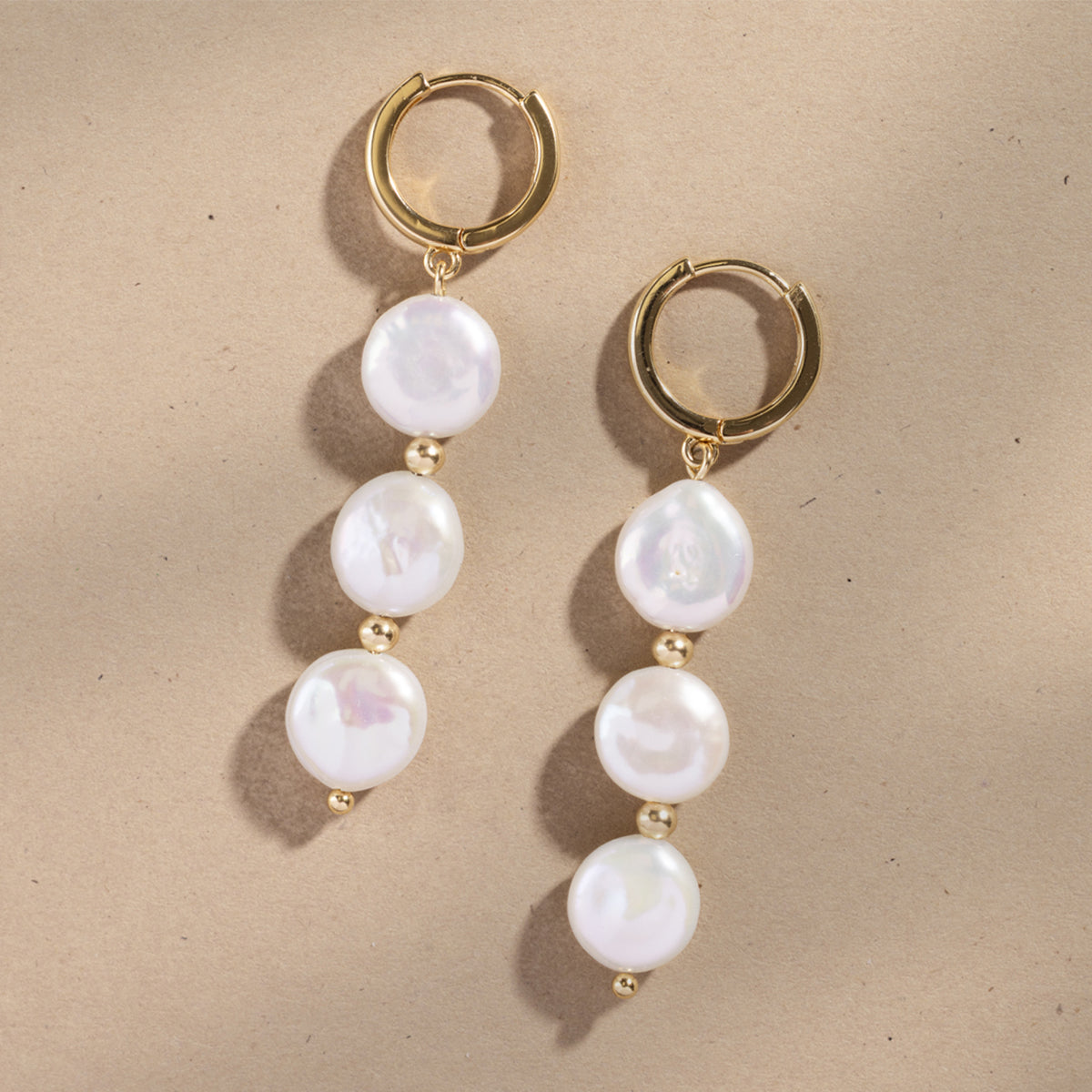Gold hoop earrings with three dangling pearls against a plain beige background.