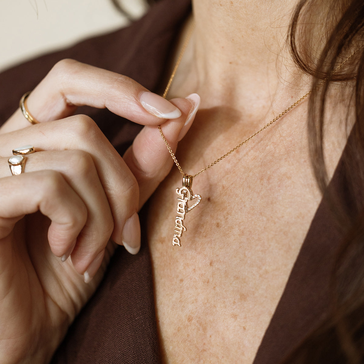 Gold necklace with 'Grandma' pendant being adjusted on a person's neck.